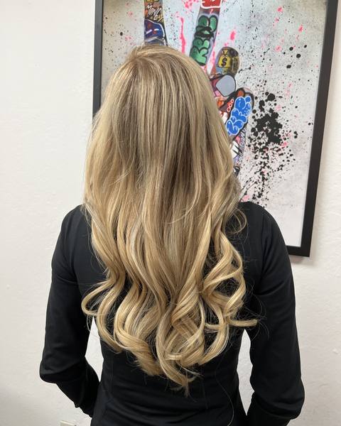 Back view of long, curled dimensional blonde highlights blended from a deeper root