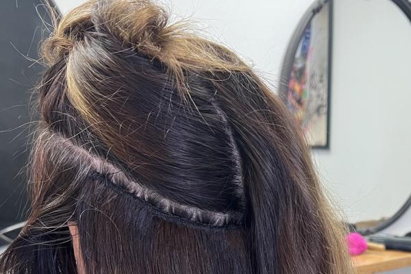 Close-up of a freshly sewn weft row along a part in a client's dark brown hair
